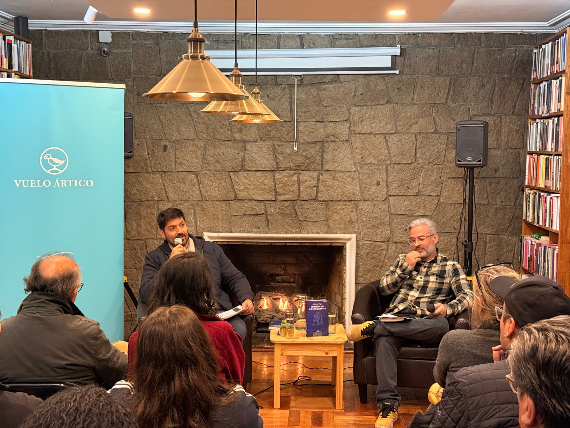 Público asistente a la presentación de Amnesia de la navegante en Librería Catalonia, con el expositor de Vuelo Ártico y la chimenea encendida al fondo